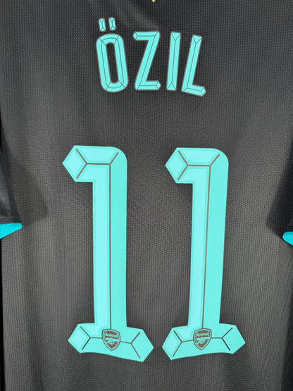Gros plan du flocage Özil N°11 cyan du maillot Arsenal 2015-2016 avec les écussons Arsenal intégrés au bas des chiffres