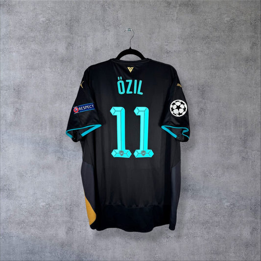 Dos du maillot Arsenal 2015-2016 third noir avec flocage Özil N°11 cyan en police Ligue des Champions, patch starball UEFA et patch RESPECT