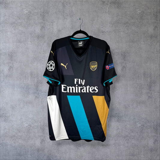 Face du maillot Arsenal 2015-2016 third Puma noir à bandes cyan, or et blanc avec sponsor Fly Emirates et patch UEFA Champions League