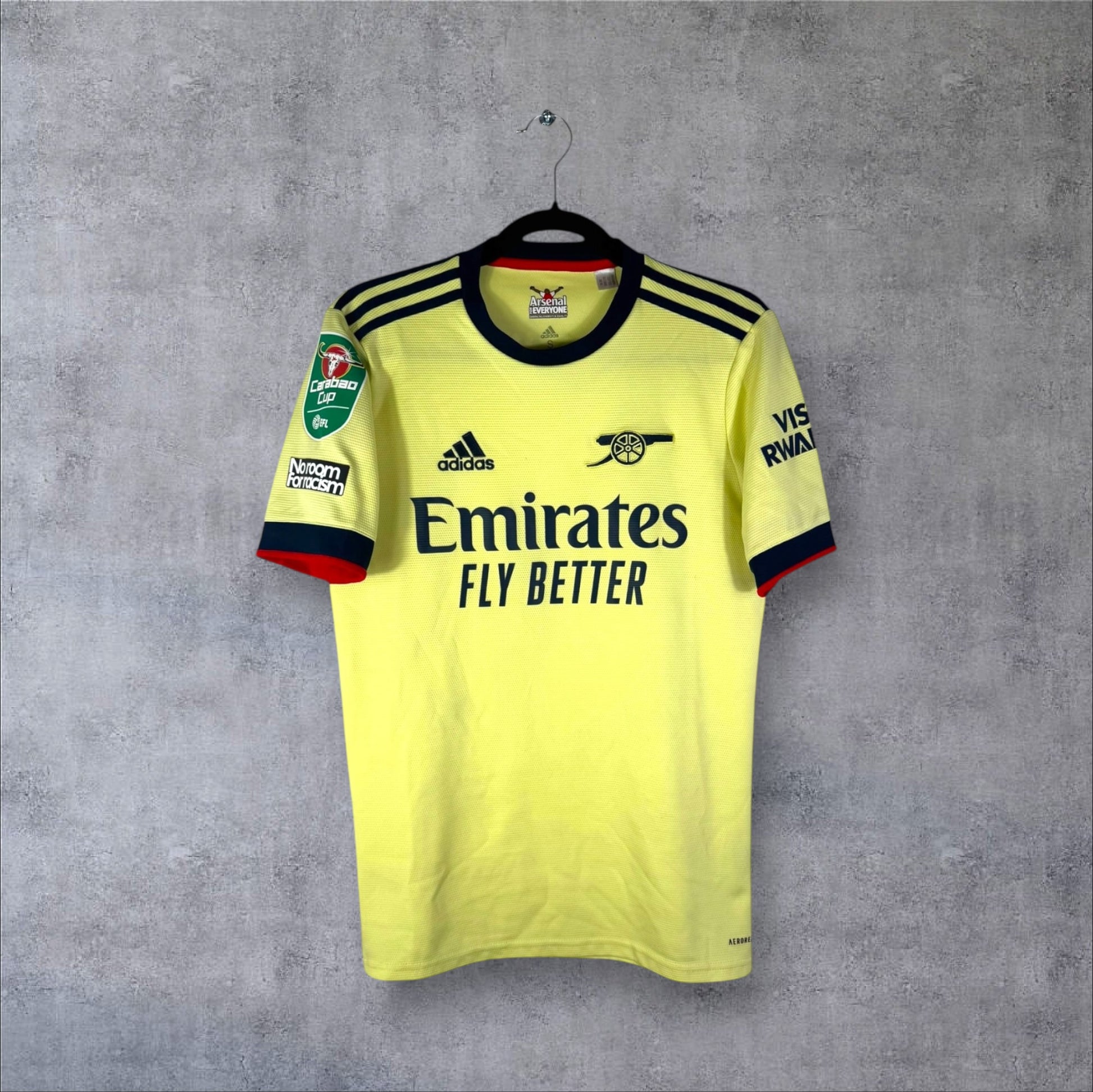Vue de face du maillot Arsenal Extérieur 2021/22 jaune perle avec logo Canon rétro bleu marine et sponsor Emirates.