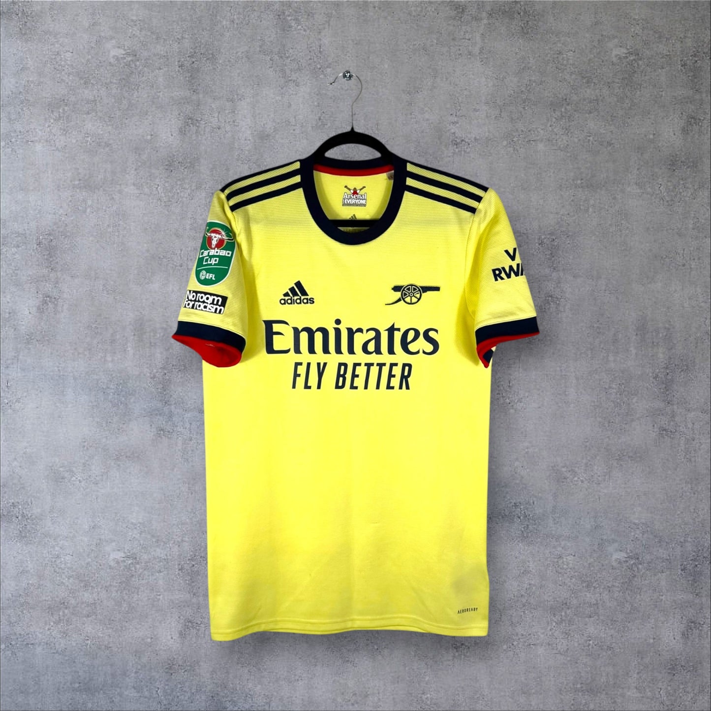 Vue de face du maillot Arsenal Extérieur 2021/22 jaune perle avec logo Canon rétro bleu marine et sponsor Emirates.