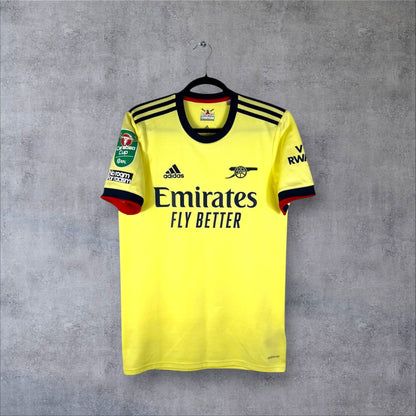 Vue de face du maillot Arsenal Extérieur 2021/22 jaune perle avec logo Canon rétro bleu marine et sponsor Emirates.