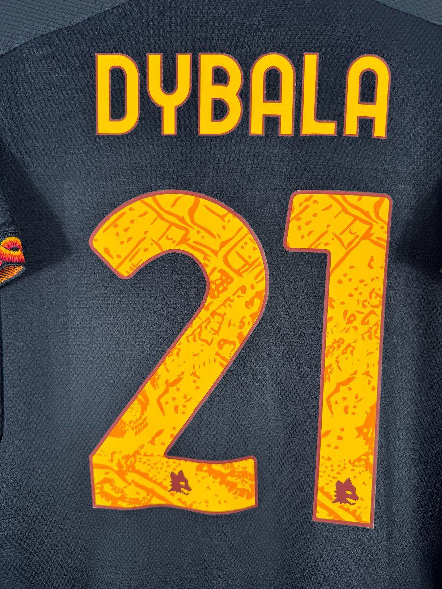 Gros plan du flocage Dybala N°21 jaune à motif romain avec têtes de loup intégrées, maillot third 2023-2024