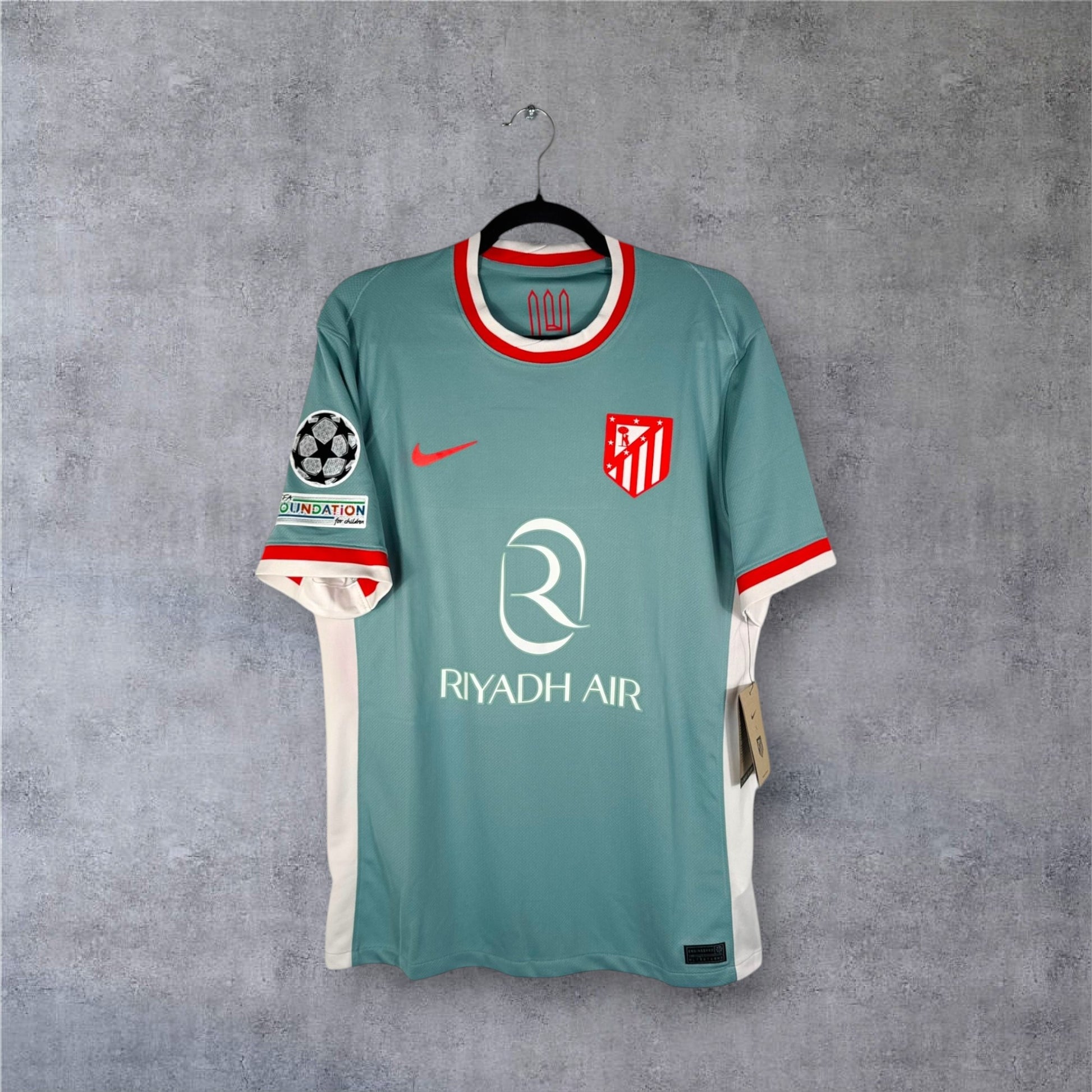 Vue de face du maillot Atletico Madrid Extérieur 2024/25 gris avec le blason classique et sponsor Riyadh Air.