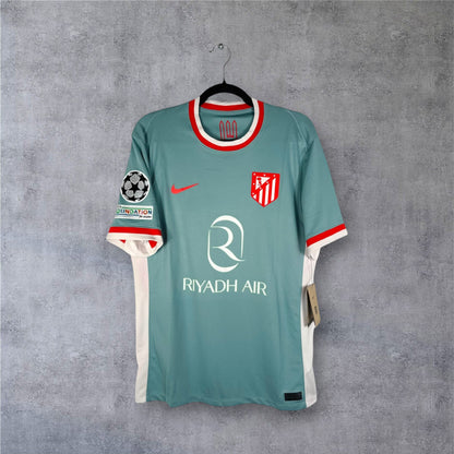 Vue de face du maillot Atletico Madrid Extérieur 2024/25 gris avec le blason classique et sponsor Riyadh Air.