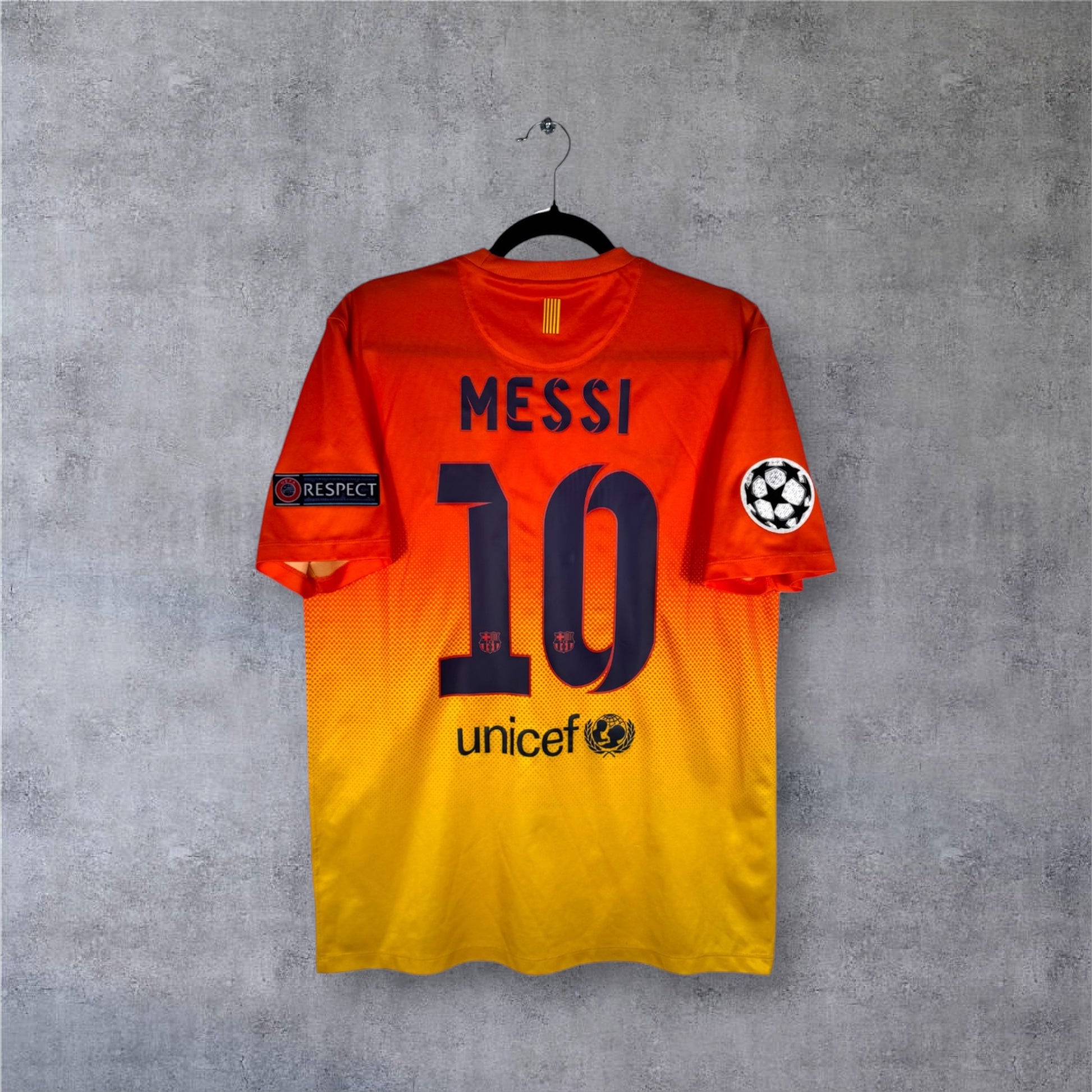 Flocage officiel bleu MESSI numéro 10 et patchs Ligue des Champions sur maillot orange Barça.
