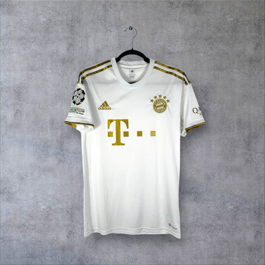 Vue de face du maillot Bayern Munich 2022/23 extérieur blanc avec logos et sponsor dorés.