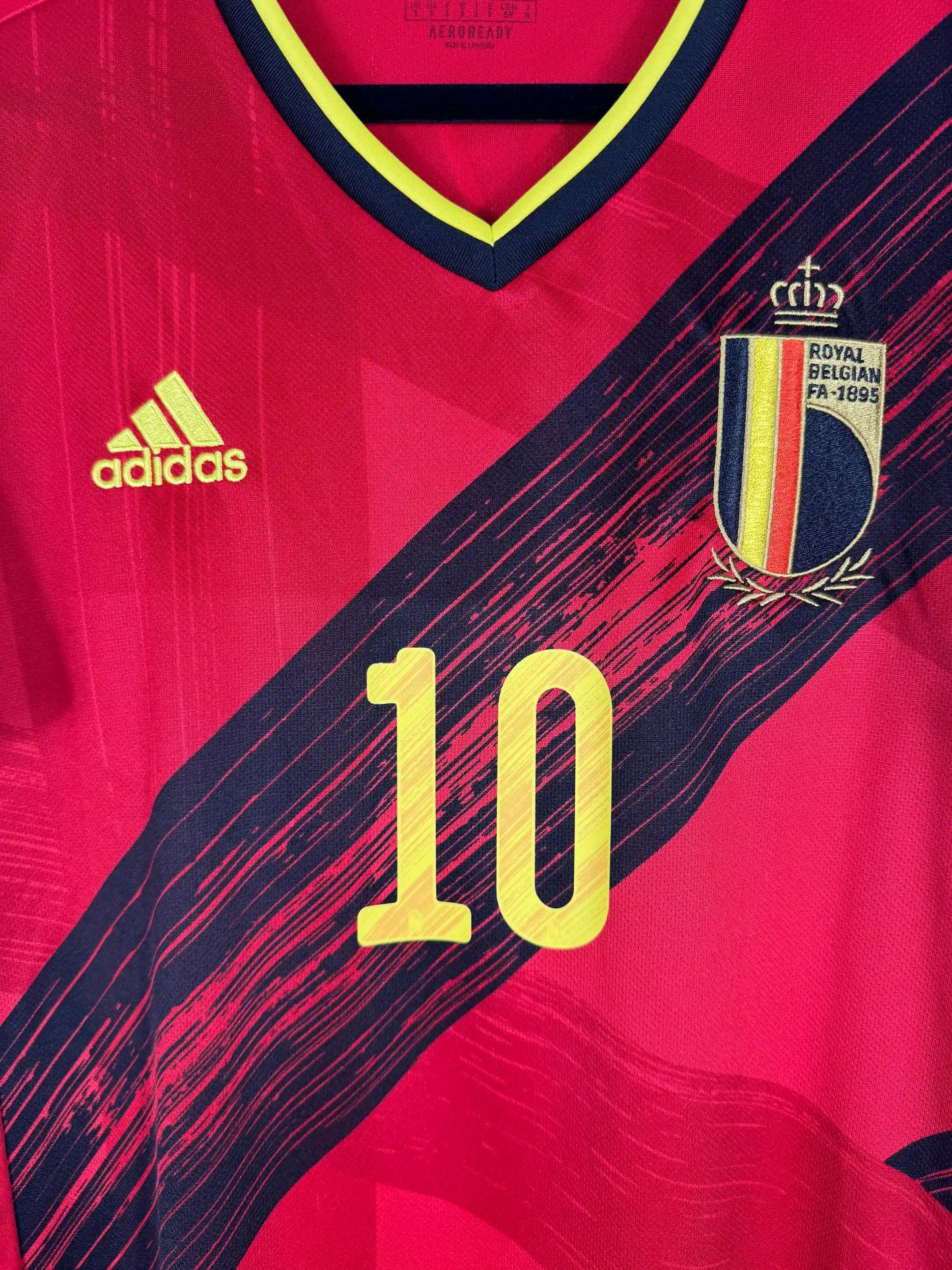 Détail écusson Royal Belgian Football Association et design diagonal tricolore belge jaune noir rouge sur maillot domicile Euro 2020 reporté COVID