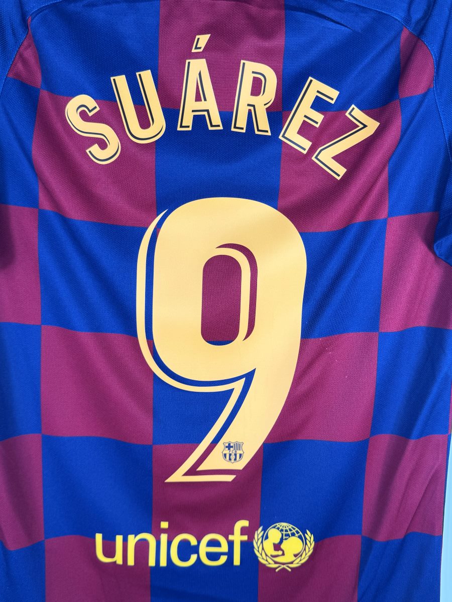 Gros plan du flocage doré SUÁREZ N°9 avec écusson du FC Barcelone intégré au chiffre