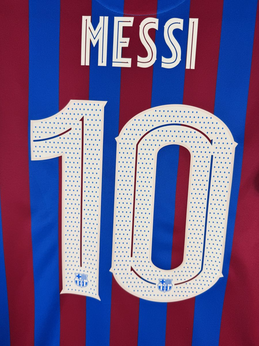 Gros plan du flocage MESSI N°10 du maillot FC Barcelone 2021-2022 en police Ligue des Champions avec les écussons du club dans les chiffres