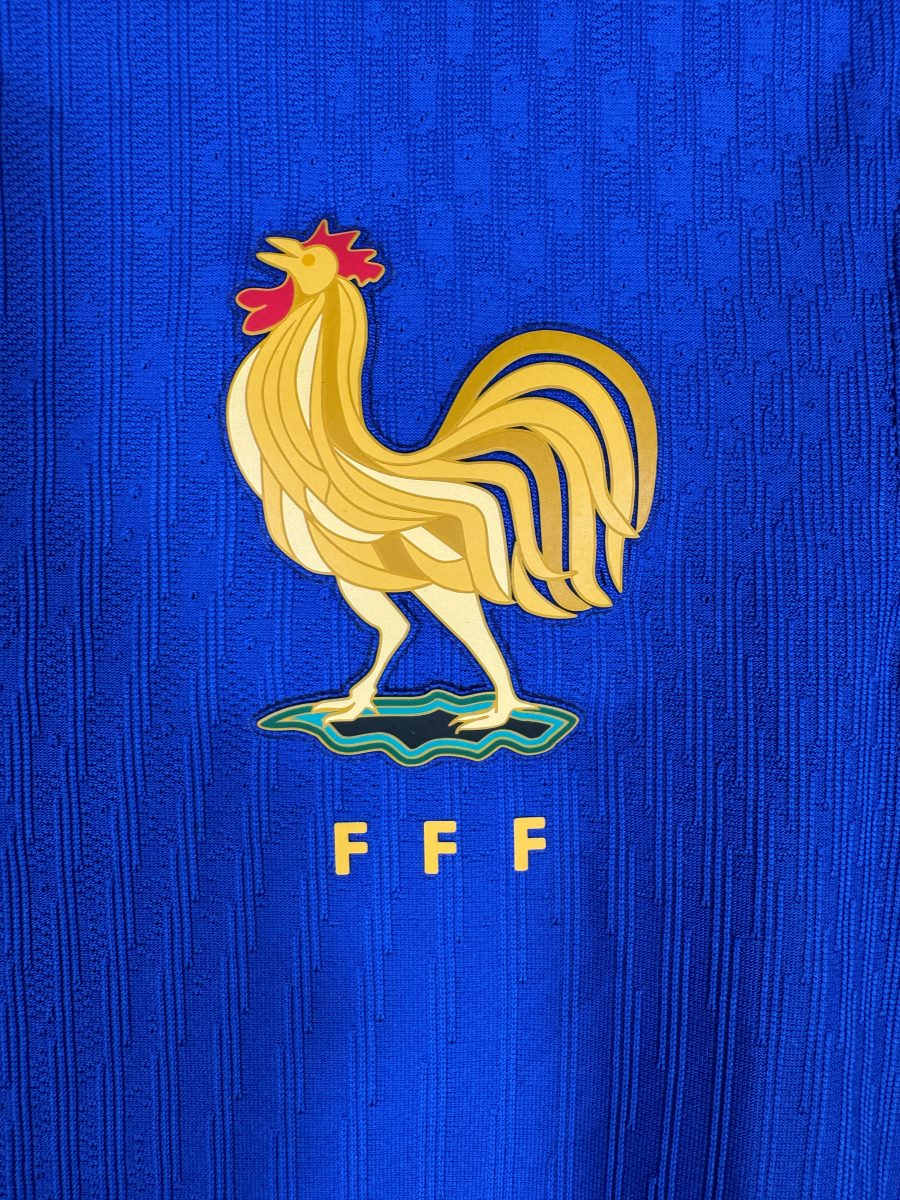 Gros plan du coq doré FFF du maillot France 2024, sans les deux étoiles : marqueur des sélections de jeunes