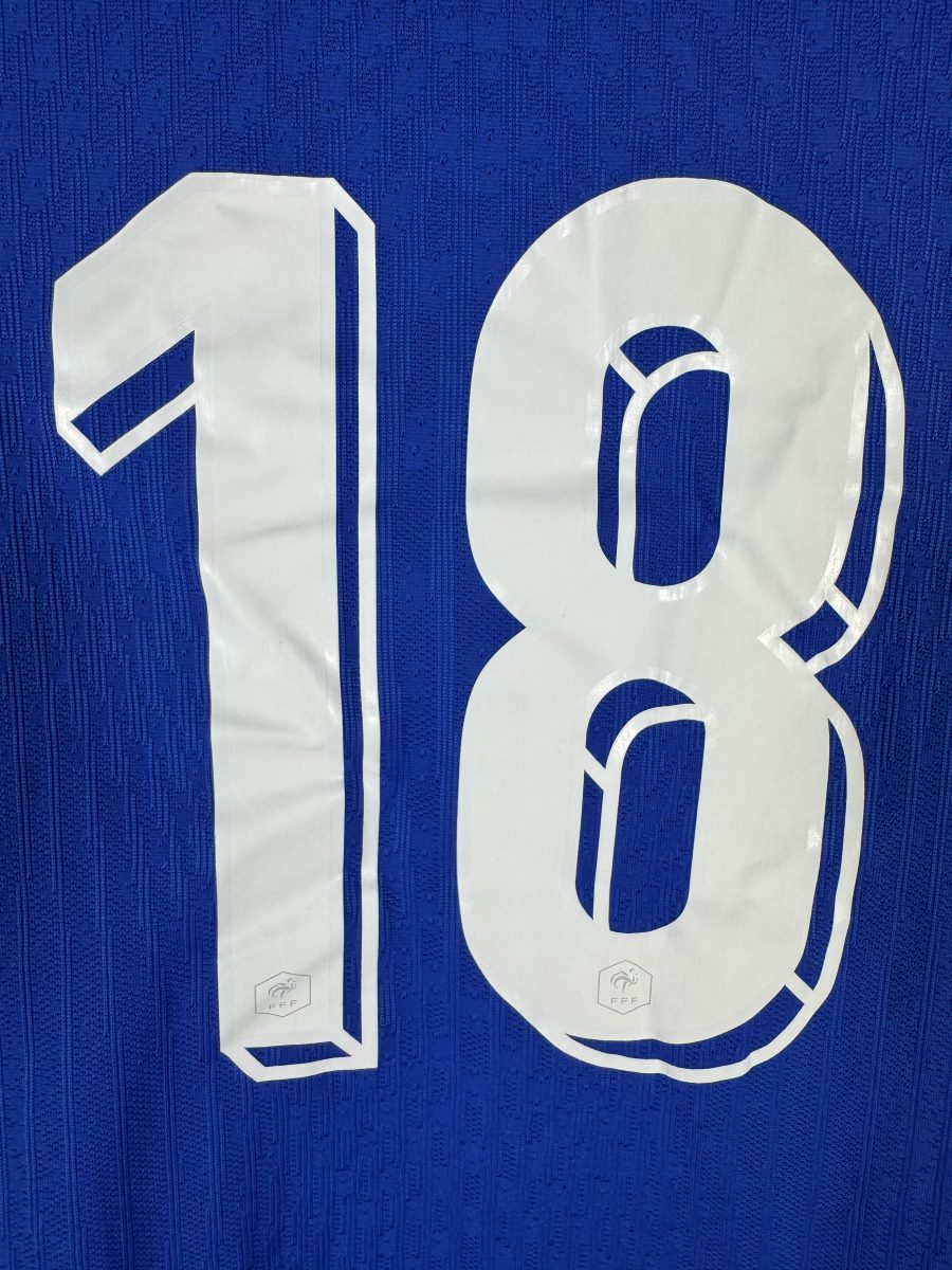 Gros plan du numéro 18 du maillot France 2024 avec les écussons hexagonaux FFF intégrés dans les chiffres