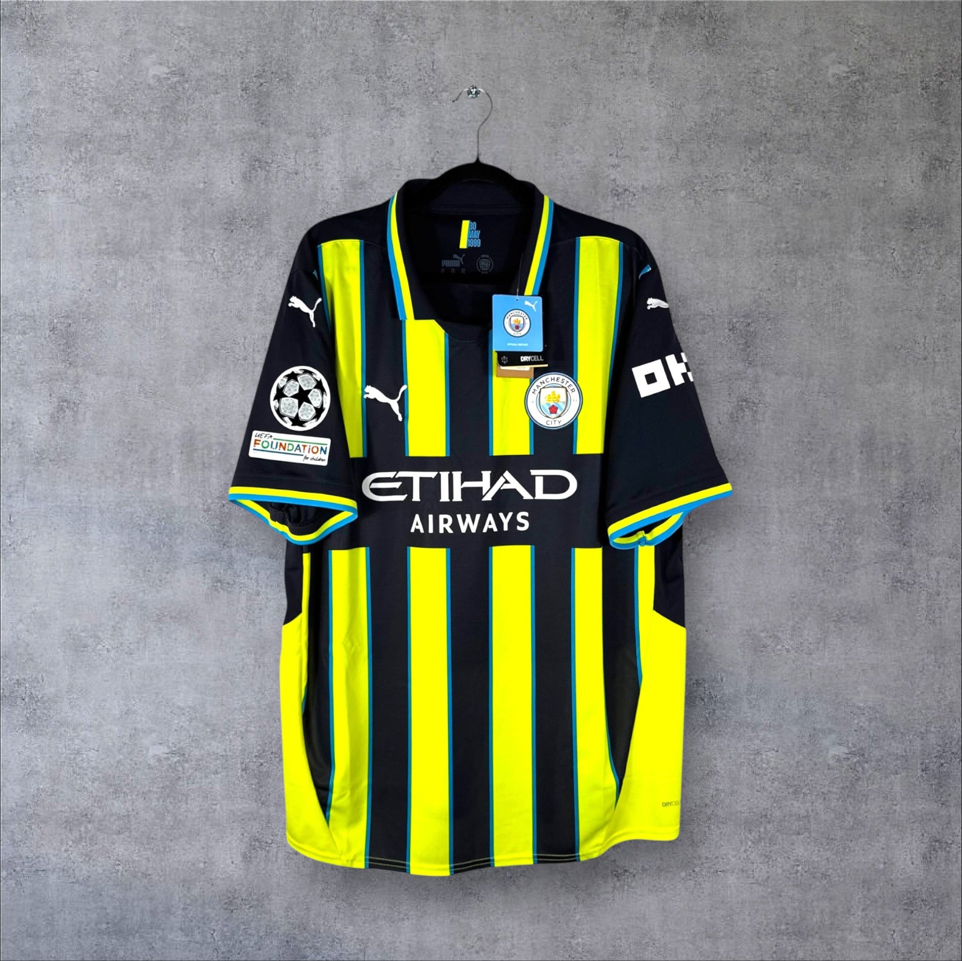 Vue de face du maillot Manchester City Extérieur 2024/25 bleu marine avec rayures jaune fluo, hommage au maillot de 1999.