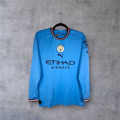 Vue de face du maillot manches longues Manchester City 2022/23 avec logos centrés.