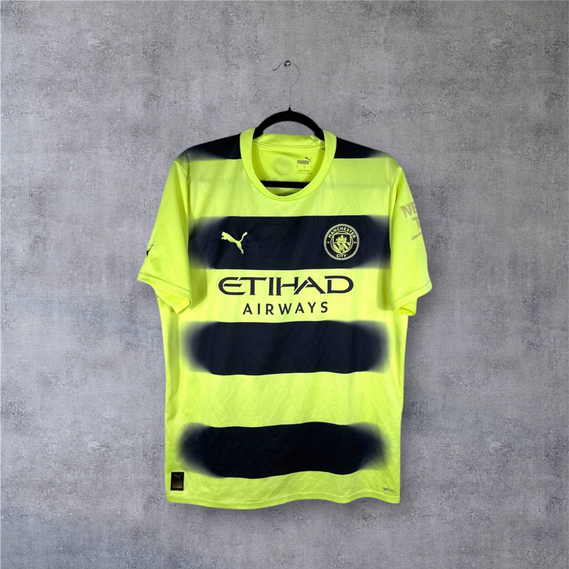 Vue de face du maillot Manchester City Third 2022/23 jaune fluo traversé par des bandes noires horizontales à effet fondu.
