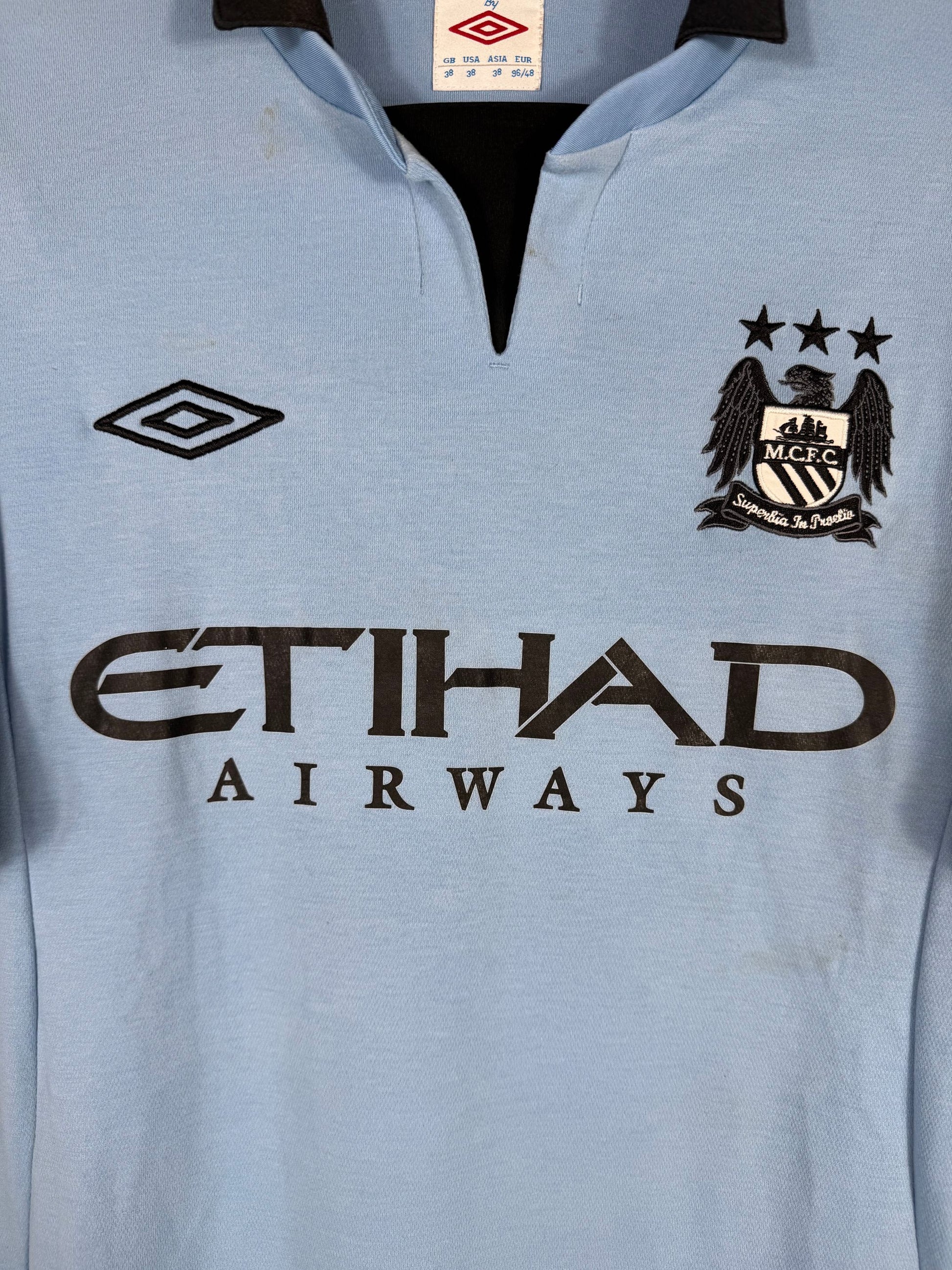Détail écusson Manchester City, double logo Umbro et sponsor Etihad Airways sur maillot domicile 2012-2013