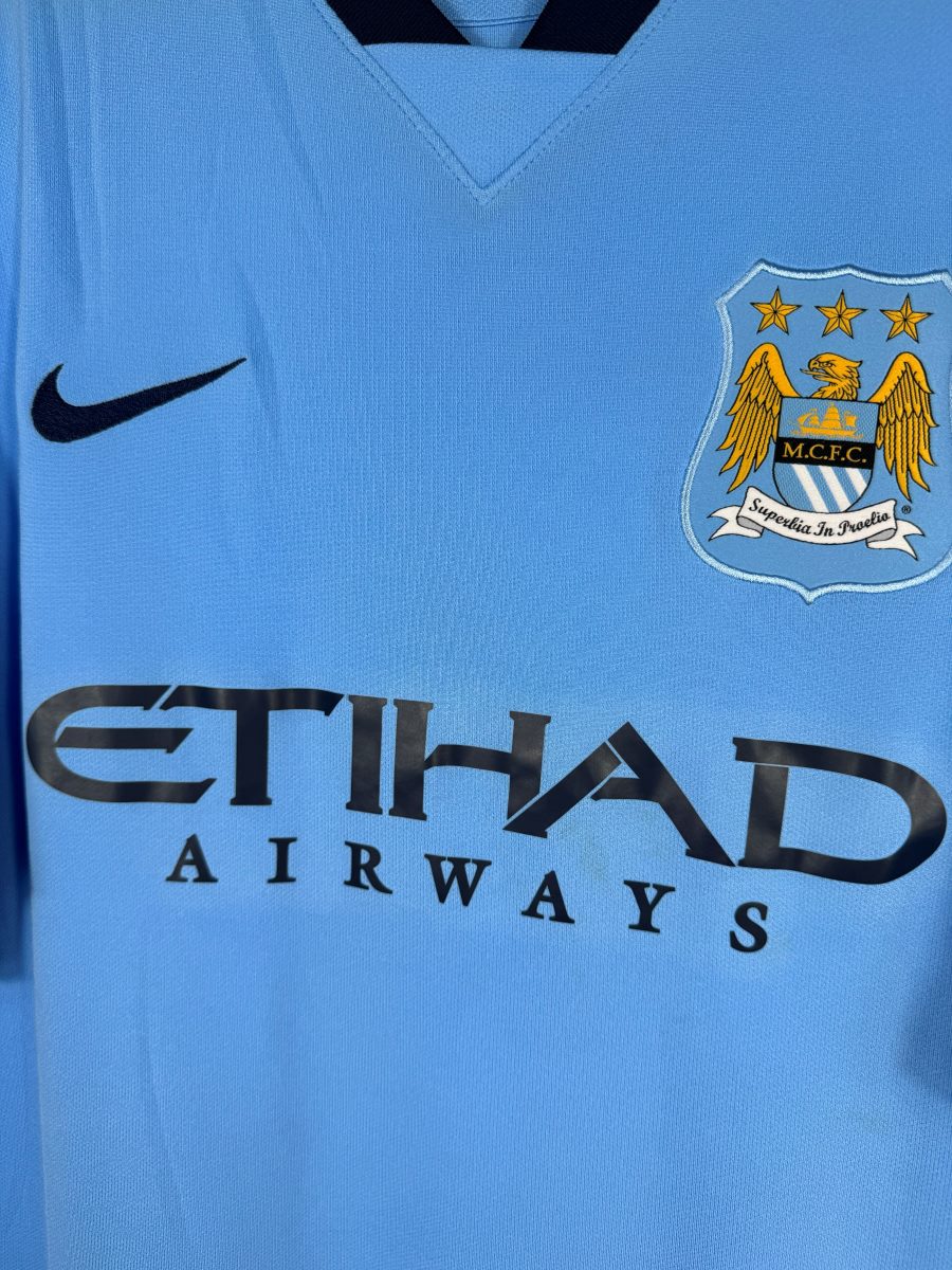 Écusson Manchester City à l'aigle brodé, swoosh Nike et sponsor Etihad, maillot domicile 2014-2015
