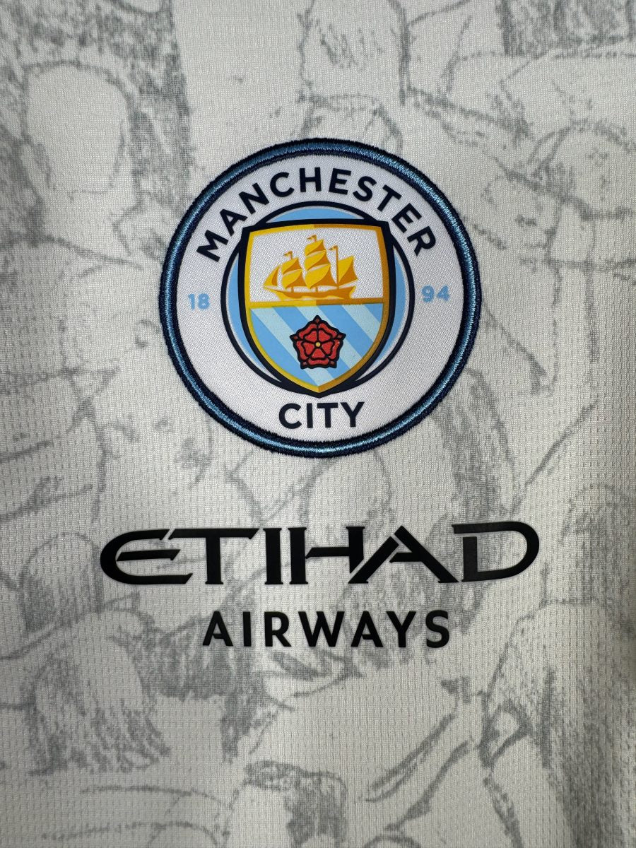Détail du blason Manchester City brodé, du sponsor Etihad Airways et des illustrations KidSuper