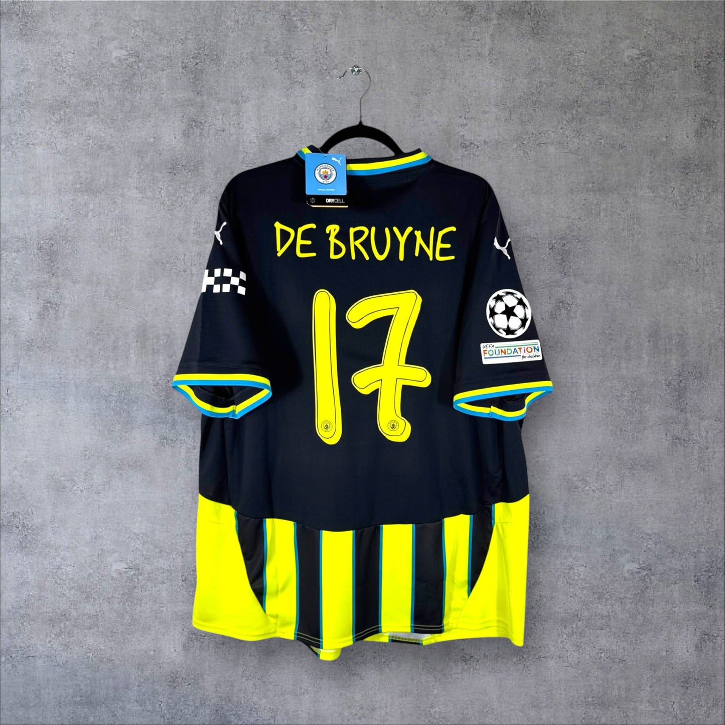 Dos du maillot Manchester City Away 2024/25 rayé jaune et bleu avec flocage DE BRUYNE 17 (police Noel Gallagher) et patchs UCL.