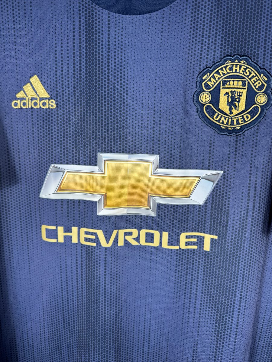 Détail de l'écusson doré brodé de Manchester United et du logo Chevrolet sur le maillot third 2018-2019