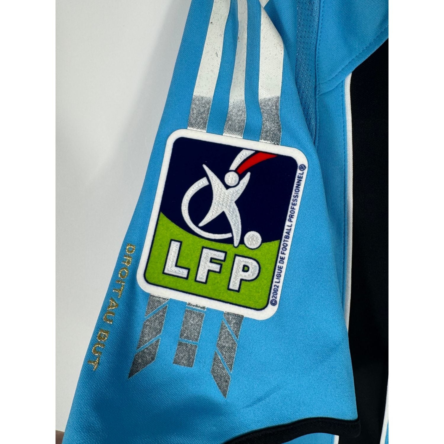 Gros plan sur les bandes Adidas endommagées et collantes sur les épaules du maillot de l'OM