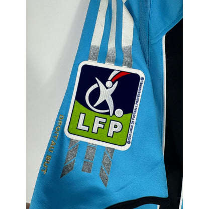 Gros plan sur les bandes Adidas endommagées et collantes sur les épaules du maillot de l'OM
