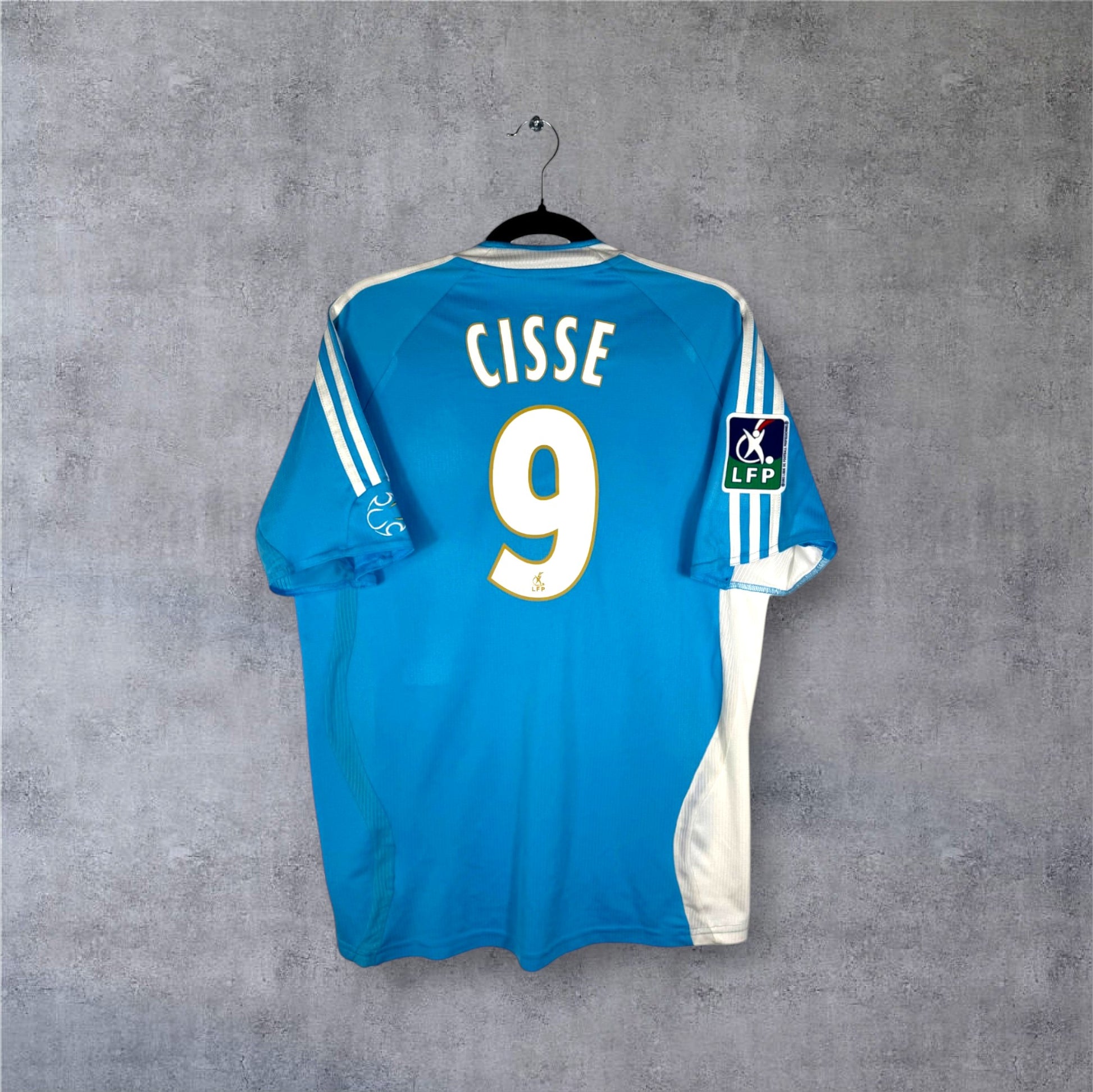 Flocage officiel CISSE numéro 9 et patch Ligue 1 sur le maillot extérieur bleu de l'OM.