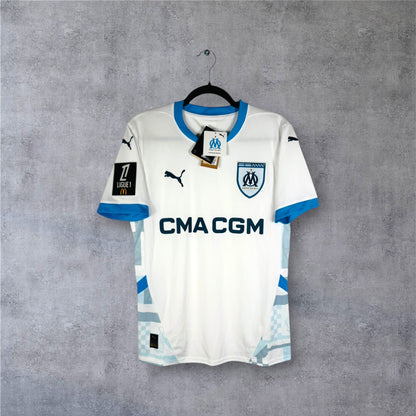 Vue de face du maillot OM 2024/25 blanc avec panneaux latéraux bleus et sponsor CMA CGM.
