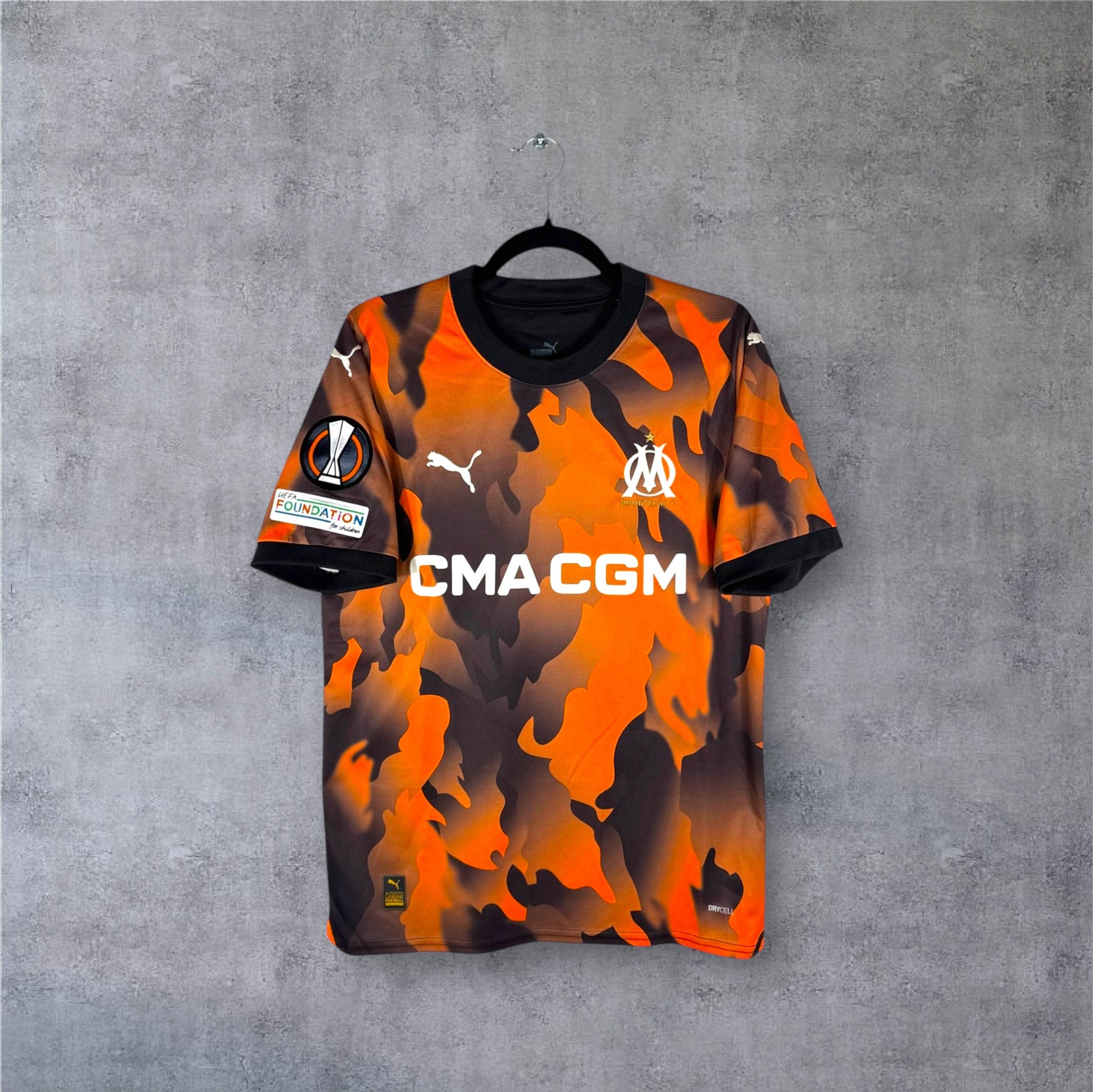 Vue de face du maillot OM 2023/24 Third noir avec motifs graphiques orange et sponsor CMA CGM.