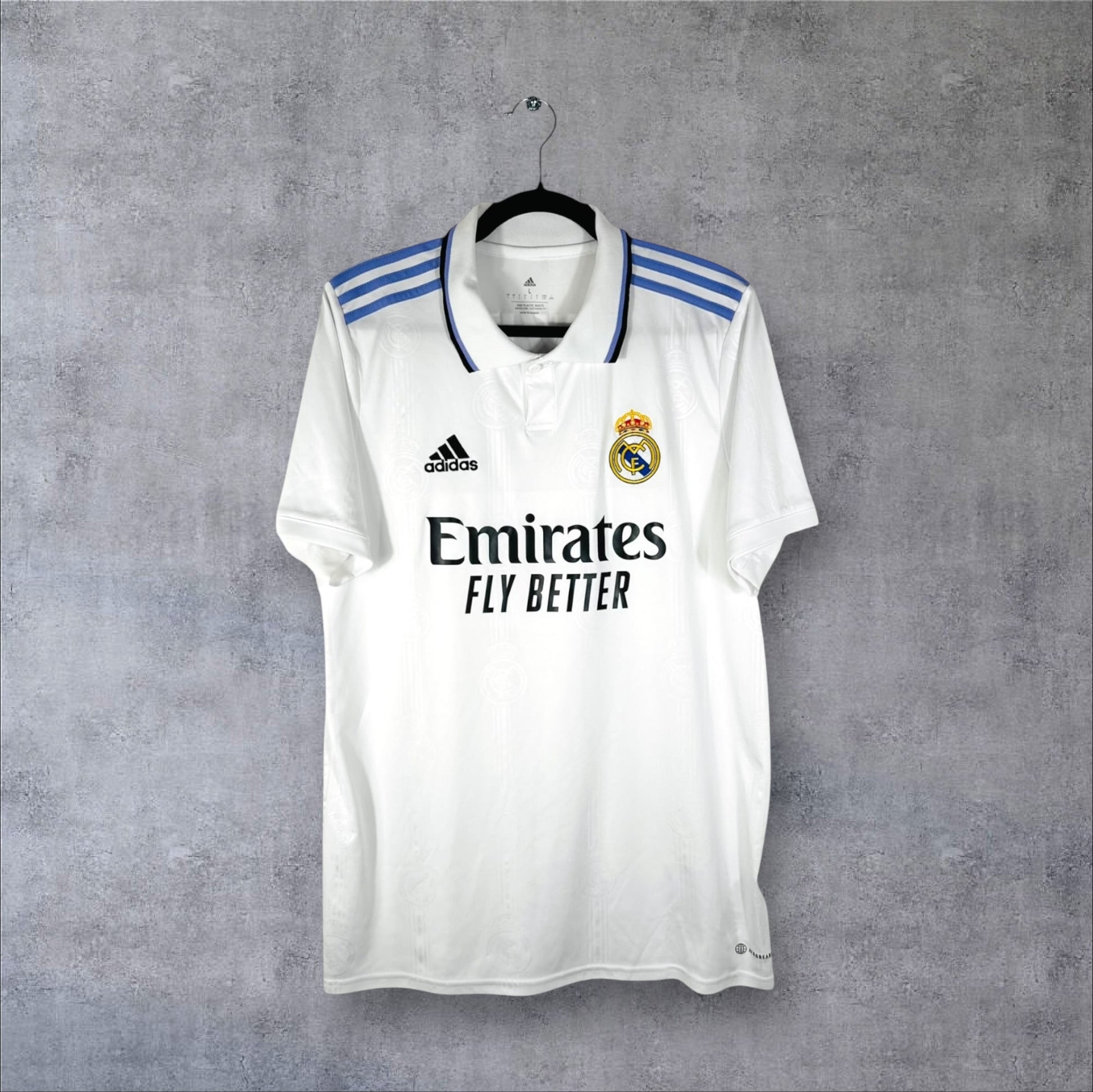 Vue de face du maillot Real Madrid 2022/23 blanc avec col boutonné et bandes Adidas violettes.