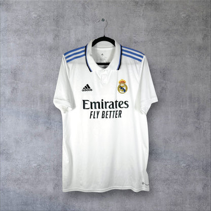 Vue de face du maillot Real Madrid 2022/23 blanc avec col boutonné et bandes Adidas violettes.
