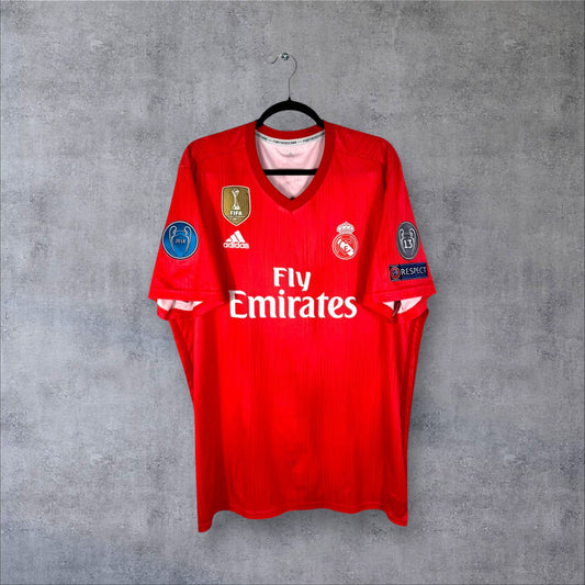 Vue de face du maillot Real Madrid 2018/19 Third rouge corail avec badge FIFA World Champions et sponsor Fly Emirates.