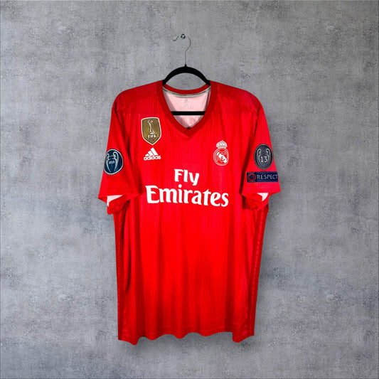 Vue de face du maillot Real Madrid 2018/19 Third rouge avec badge FIFA World Champions et sponsor Fly Emirates.