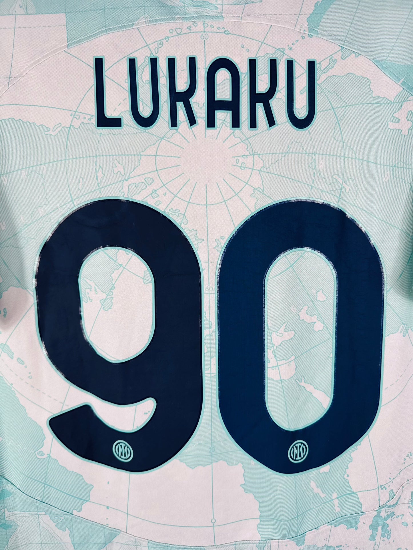 Zoom sur le numéro 90 bleu marine de Romelu Lukaku avec typographie officielle Ligue des Champions de l'Inter Milan.