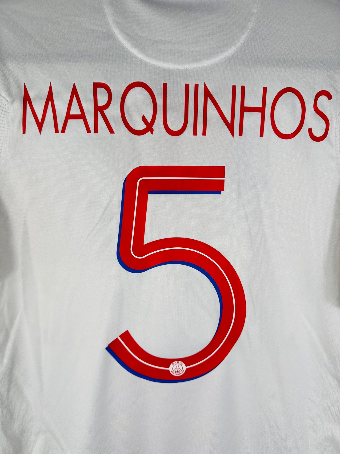 Détail du nom MARQUINHOS et du numéro 5 rouge avec liseré bleu sur le dos du maillot.